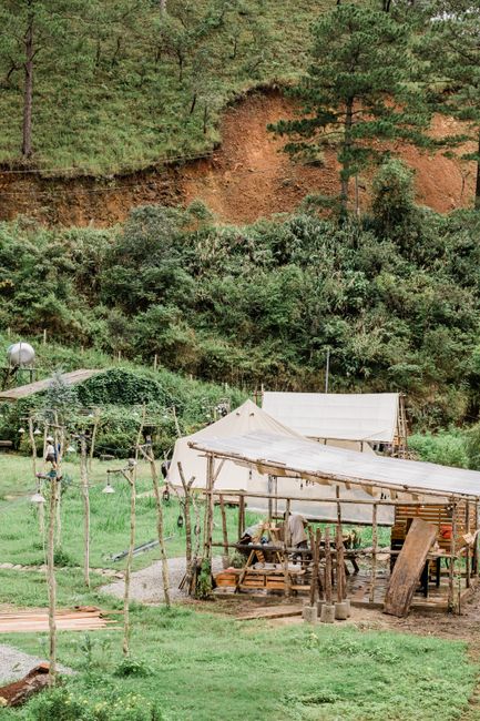 A rural area with wooden shelters set against a lush green hillside landscape.