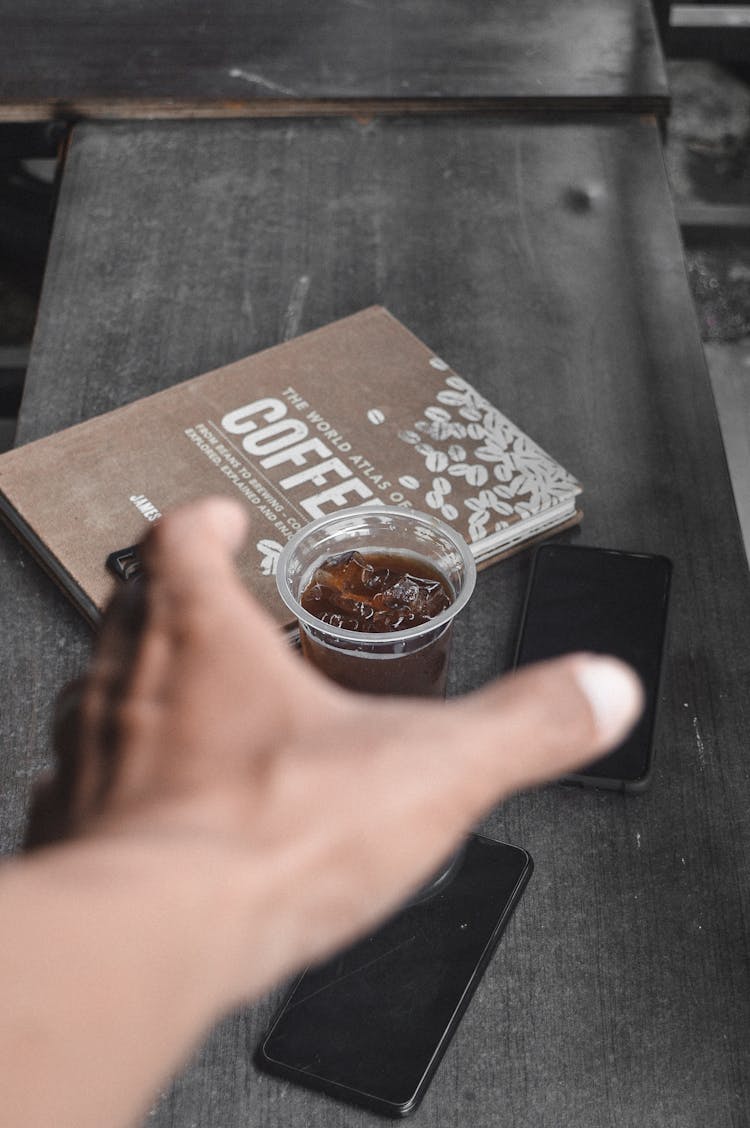 A Person Reaching An Iced Coffee On The Table