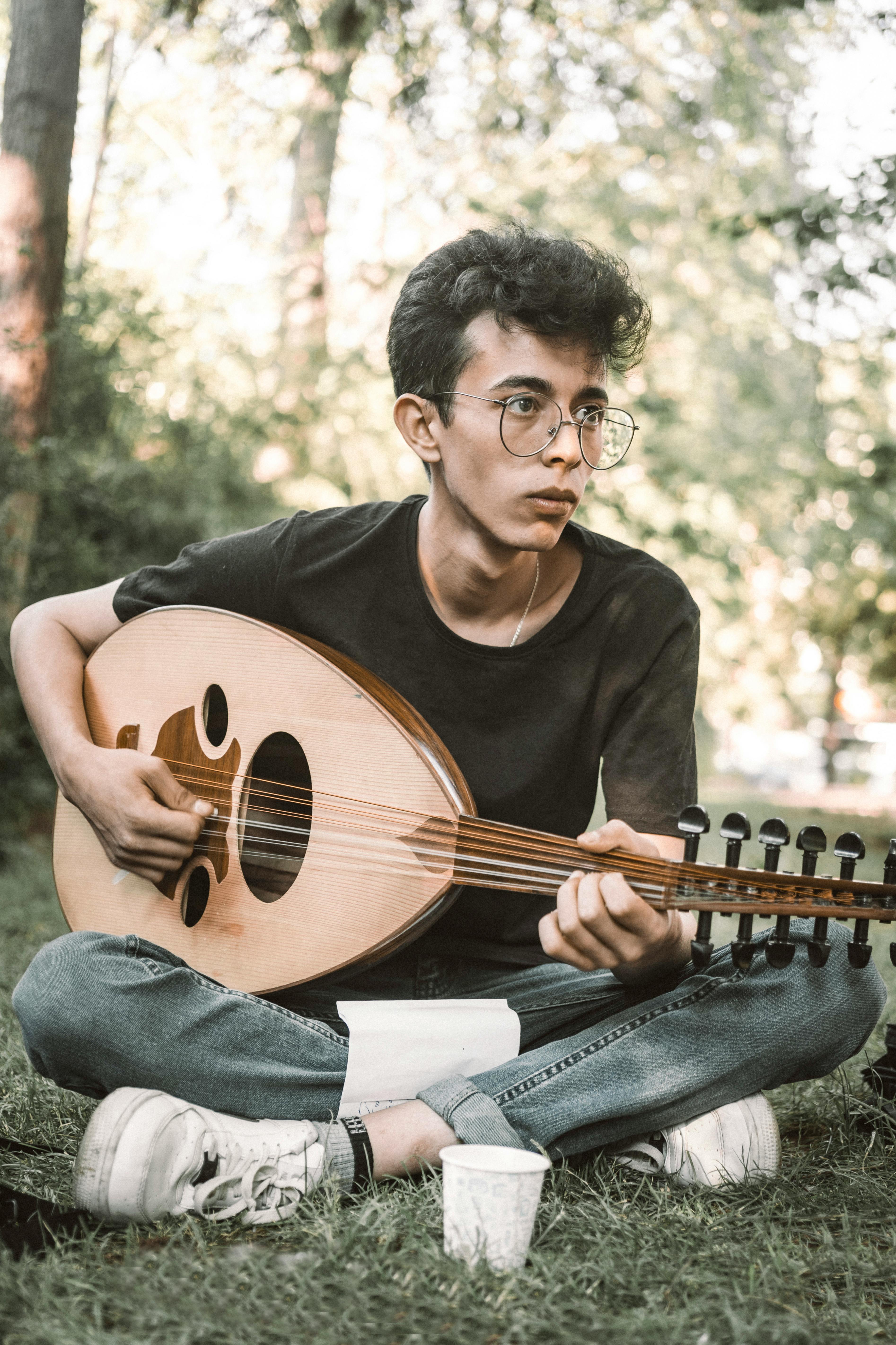 Free A Man Playing the Oud While Sitting on the Grass  Stock Photo