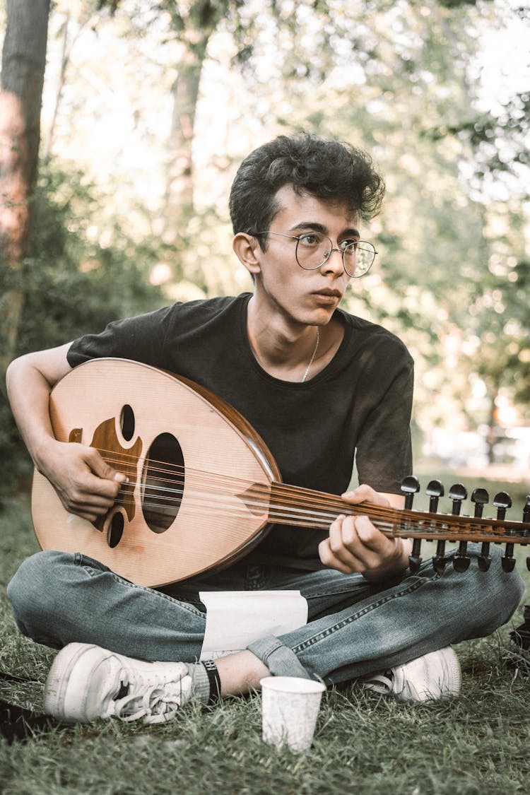 A Man Playing The Oud While Sitting On The Grass 