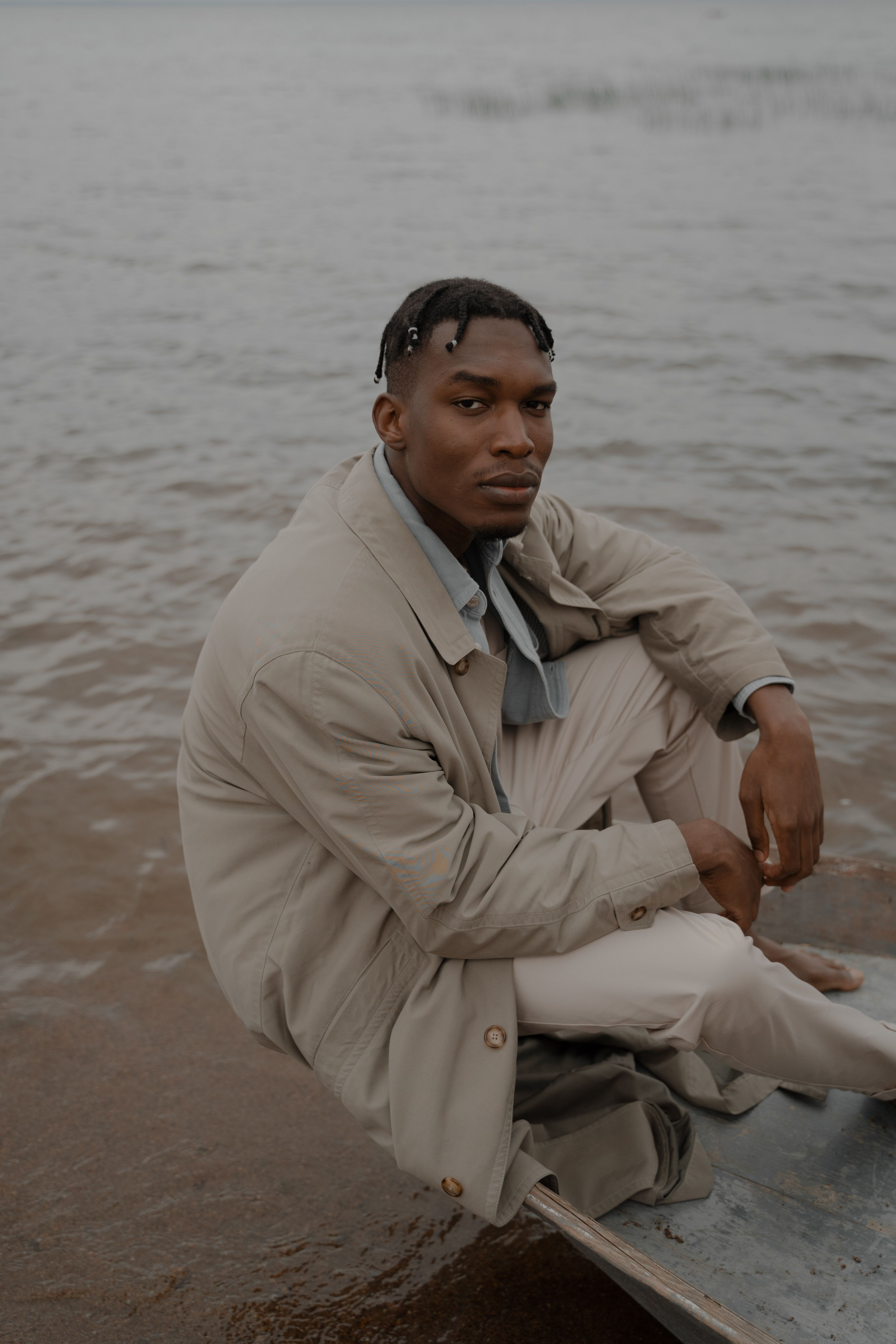 A serene portrait of a stylish man sitting on a boat at the beach, exuding fashion and relaxation.