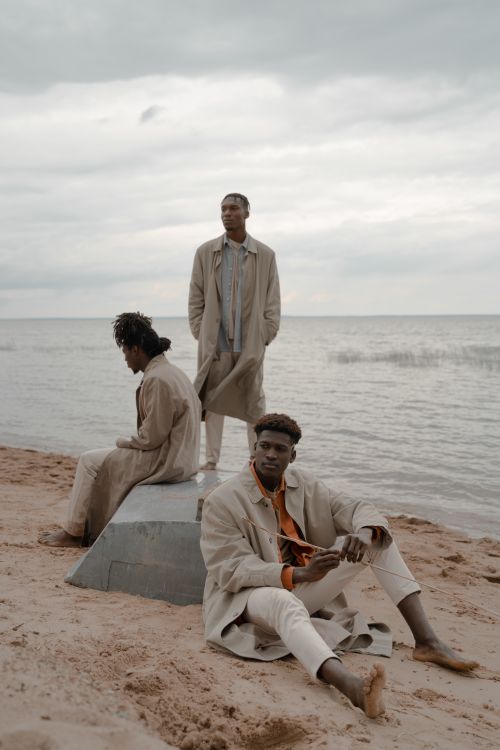 Free Three fashionable men in trench coats enjoying a peaceful day on an overcast beach. Perfect for lifestyle concepts. Stock Photo
