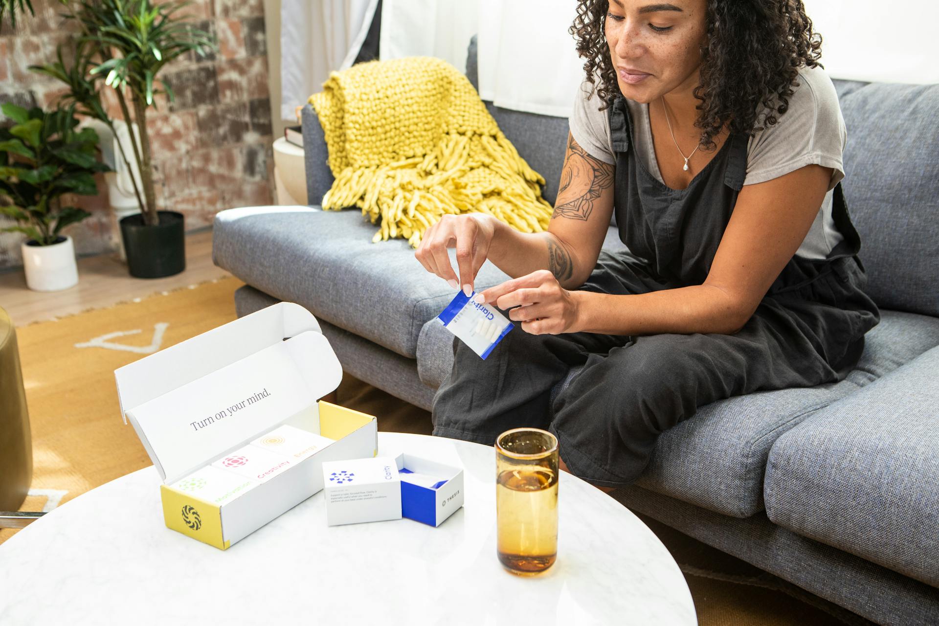 A woman seated on a sofa prepares to use dietary supplements for health and wellness at home.