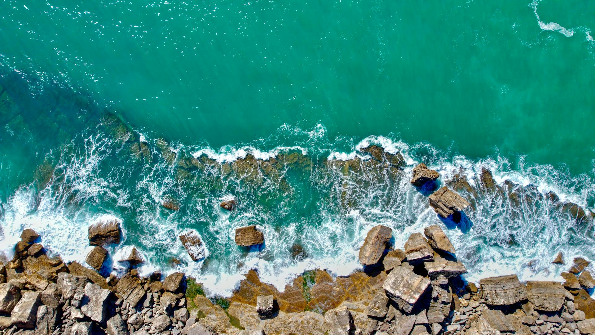 Stunning top view of Cascais rocky shoreline with waves crashing against the turquoise sea.
