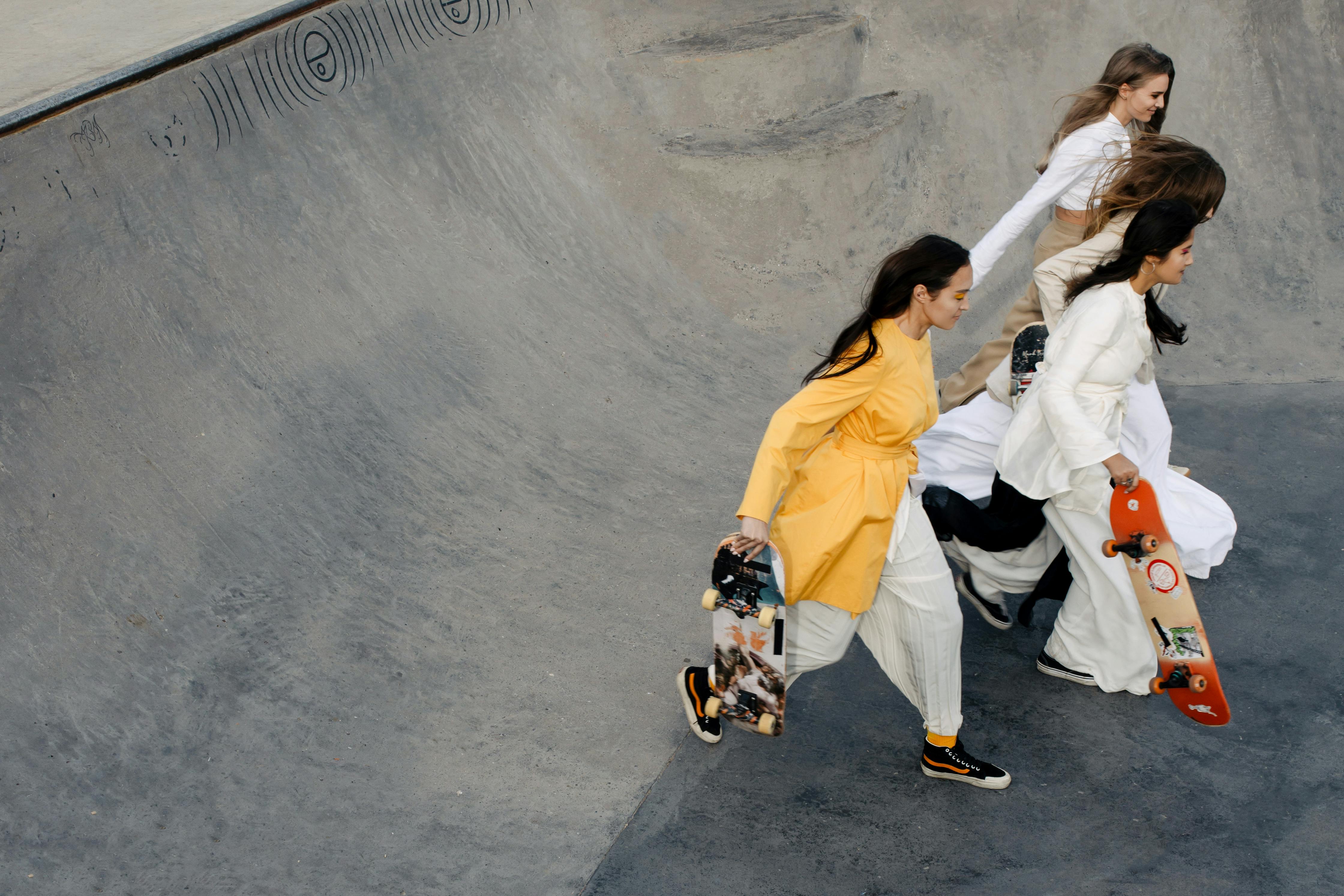 group of friends in long sleeve blouses holding skateboards running on skate ramp