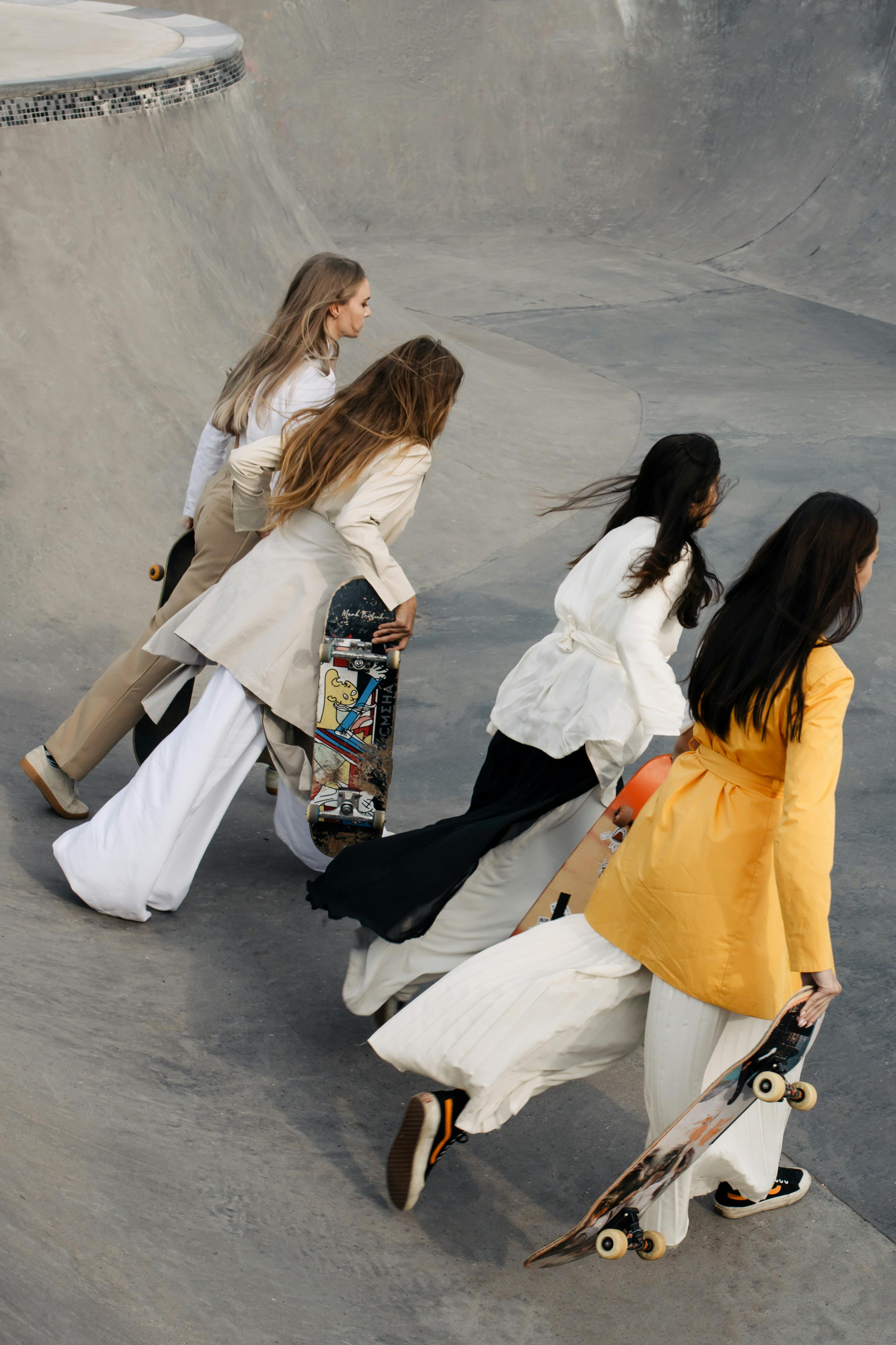 Four stylish women skateboarding together in a skate park, showcasing friendship and fashion outdoors.