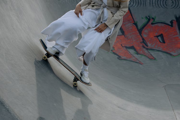 A Person In White Dress And Trench Coat Riding On A Skateboard While Doing Tricks On A Ramp