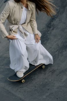 A person skateboards on a ramp wearing a fashionable white outfit and trench coat.
