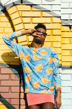 时尚模特穿着鲜艳服装，在阳光下靠在彩色砖墙上摆姿势