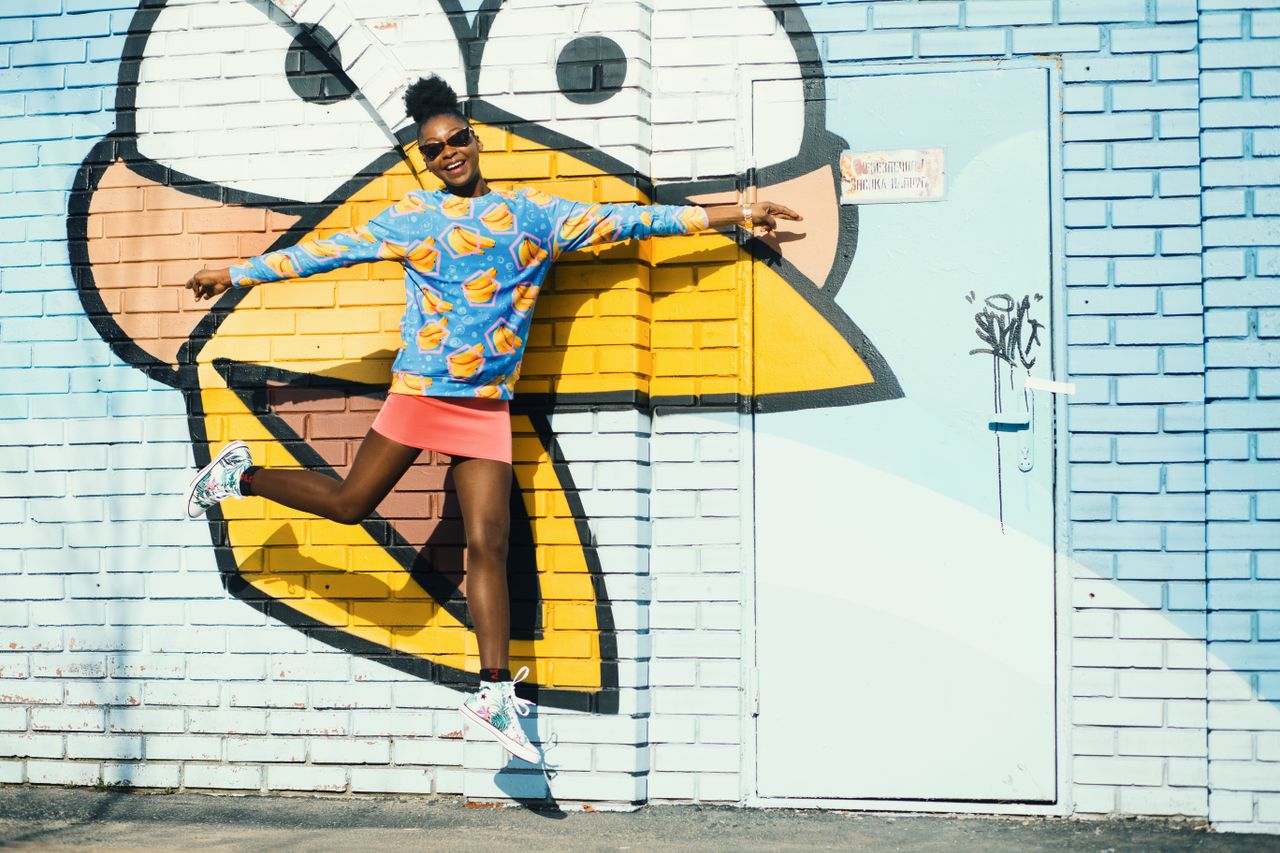 a young woman jumps happily in front of a vibrant graffiti wall featur
