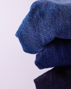 Stack of folded blue denim jeans on a white background showcasing texture and color variation.