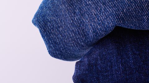 Stack of folded blue denim jeans on a white background showcasing texture and color variation.
