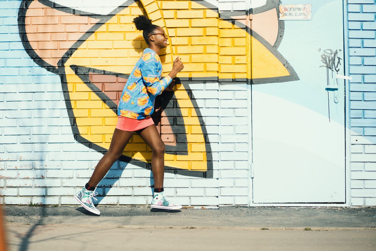 a young woman in vibrant attire running past a colorful graffiti cover