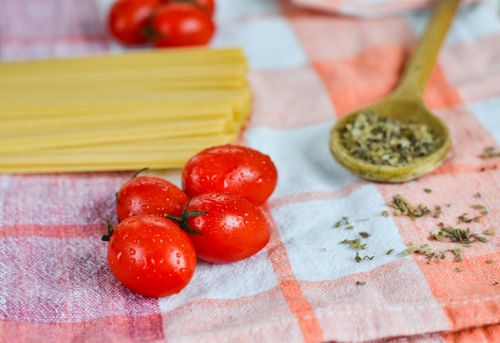 Free Fresh cherry tomatoes on a checkered cloth with pasta and herbs, perfect for Italian cuisine. Stock Photo