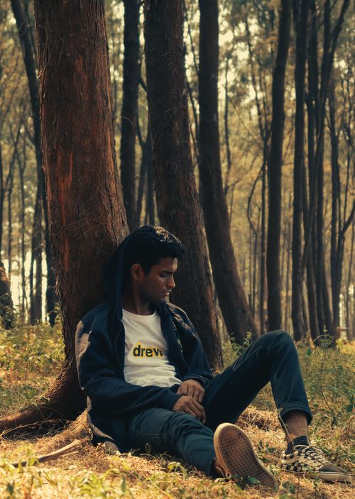 Free A young man in a hoodie sleeping under a tree in a serene forest setting. Stock Photo