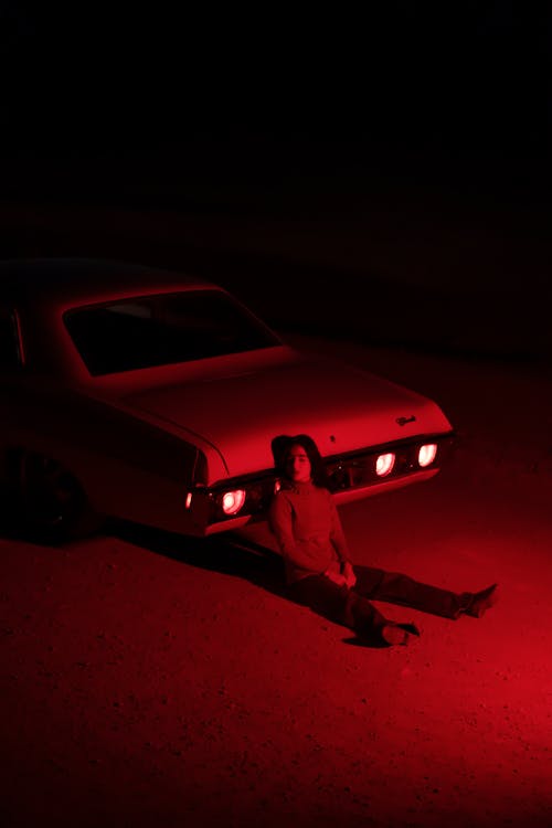 Woman Sitting on the Ground and Leaning on a Car