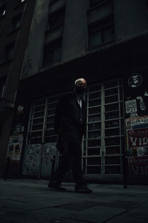Free Dark urban scene of a masked man walking on a graffiti-covered sidewalk. Stock Photo