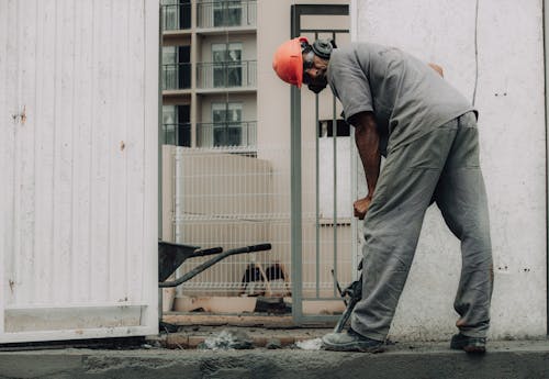 A Man Wearing Orange Helmet Drilling the Road