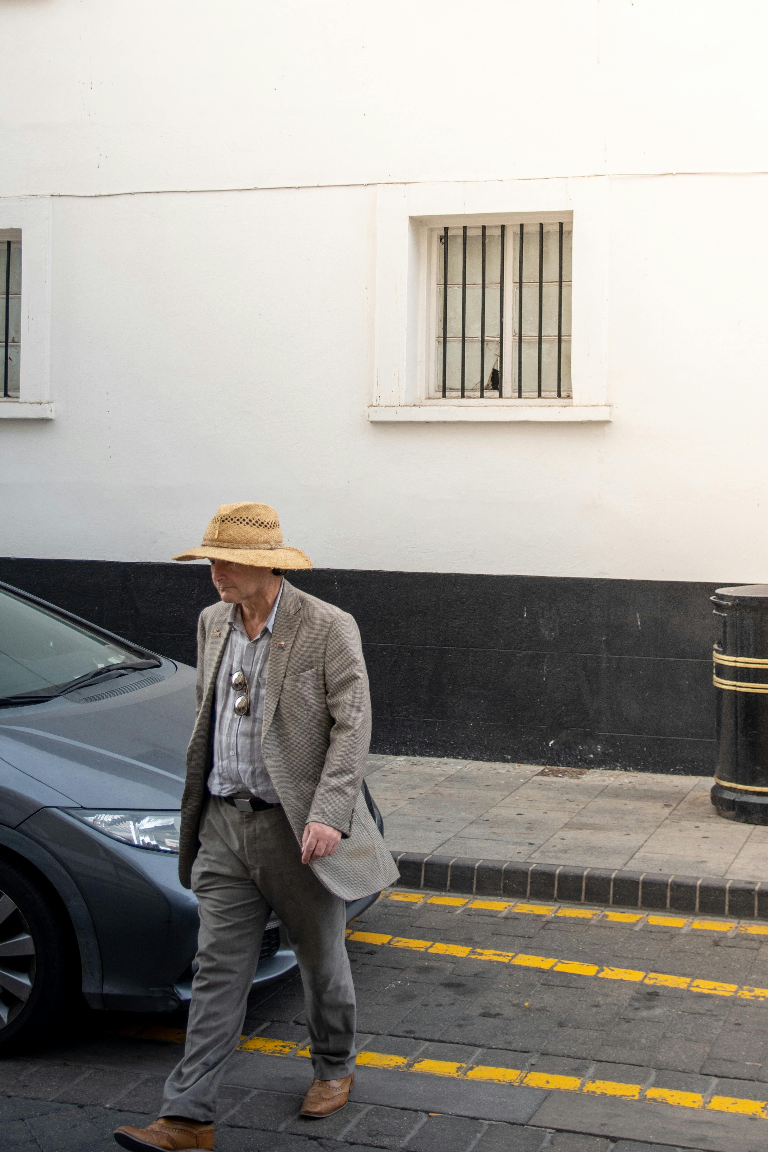 Senior man in a hat and suit walking on a sunny Marbella street, Spain.