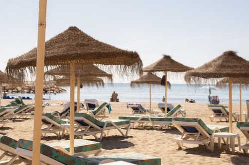 Free Idyllic sunny beach scene with straw umbrellas and loungers, perfect for a summer vacation. Stock Photo
