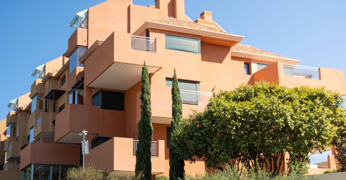 A modern Mediterranean-style apartment building with terracotta walls and lush vegetation under a clear sky.