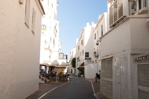 A serene whitewashed alley in Spain with outdoor dining on a sunny day.