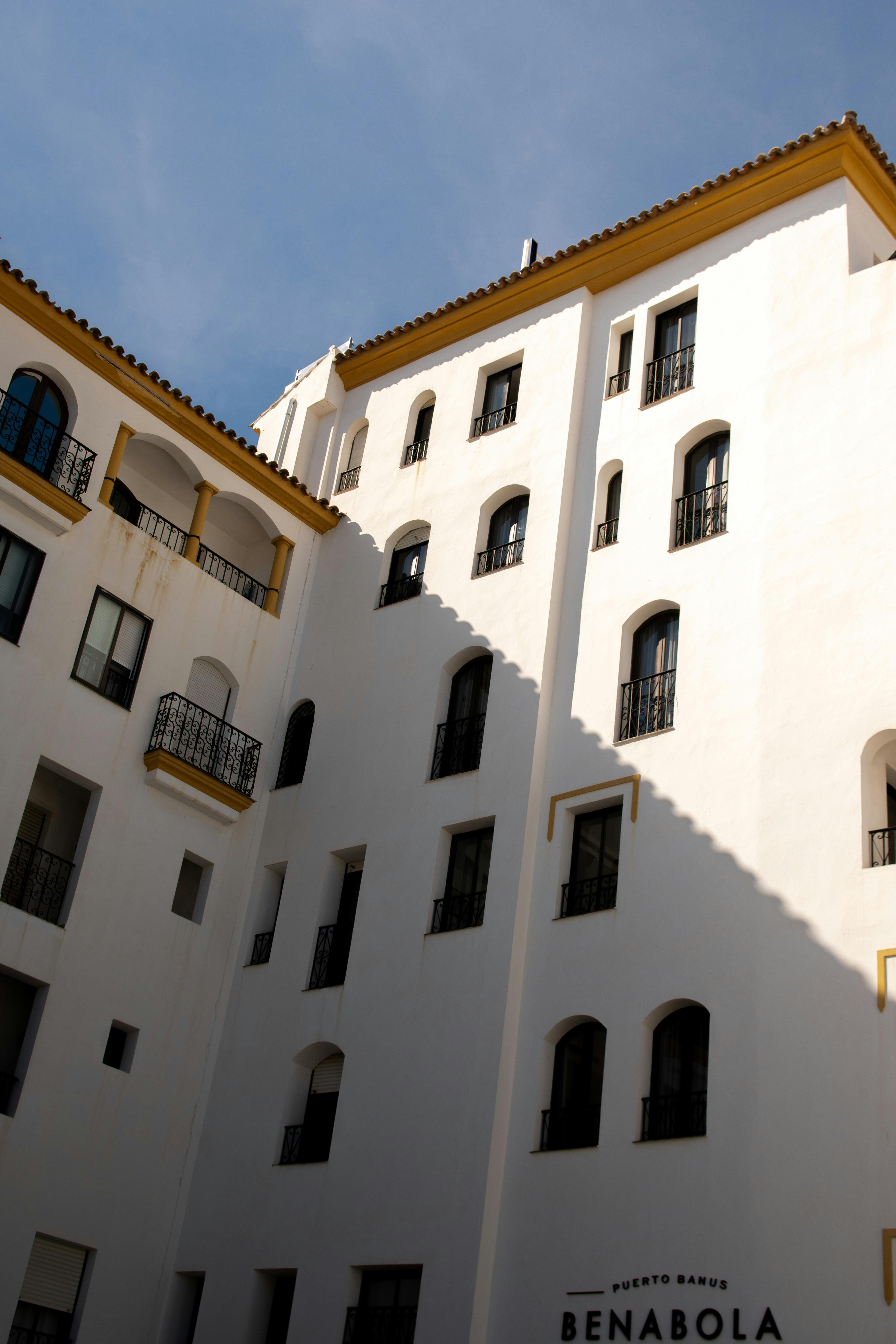 White facade of Spanish hotel with multiple balconies and windows in bright daylight.