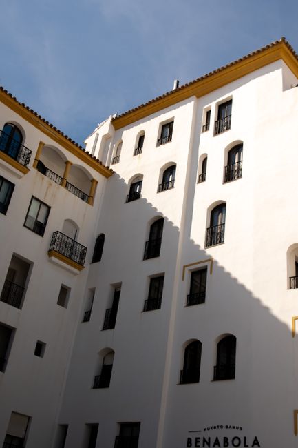 White facade of Spanish hotel with multiple balconies and windows in bright daylight.