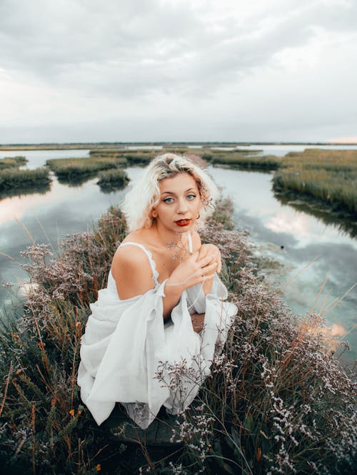 Free Woman in White Spaghetti Strap Dress Standing on Green Grass Field Near Lake Stock Photo