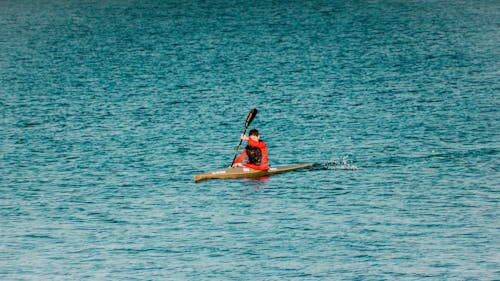 Person in Orange Long Sleeves Kayaking on the Blue Sea 