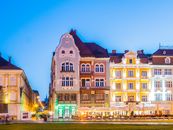 Illuminated historic buildings with vibrant facades in Timișoara's city center during evening time.