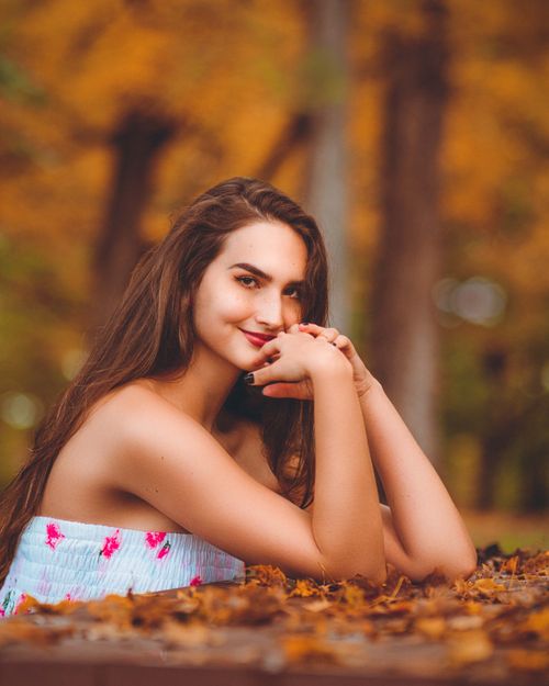 Free Smiling woman in a fall forest with a vibrant tube top, surrounded by leaves. Stock Photo