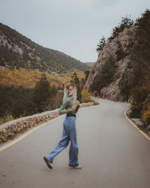 Free A Woman in Green Long Sleeves and Denim Pants Walking on the Road Stock Photo