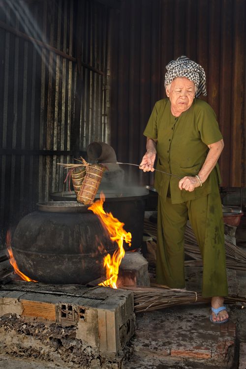 Free Senior woman cooking over an open flame in a traditional setting, capturing cultural heritage. Stock Photo