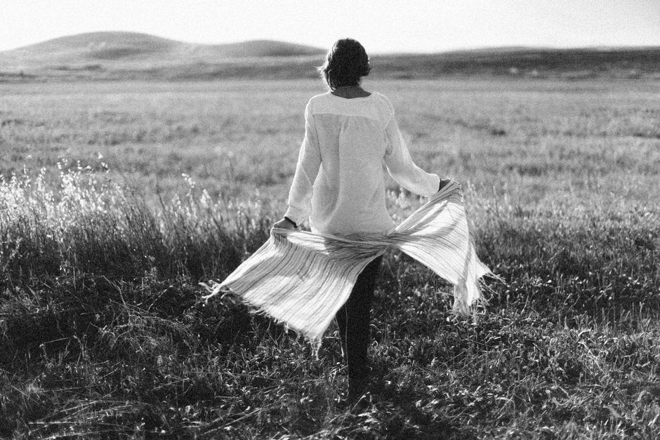 Black and white photo of a woman walking through a tranquil field, showcasing a peaceful moment.