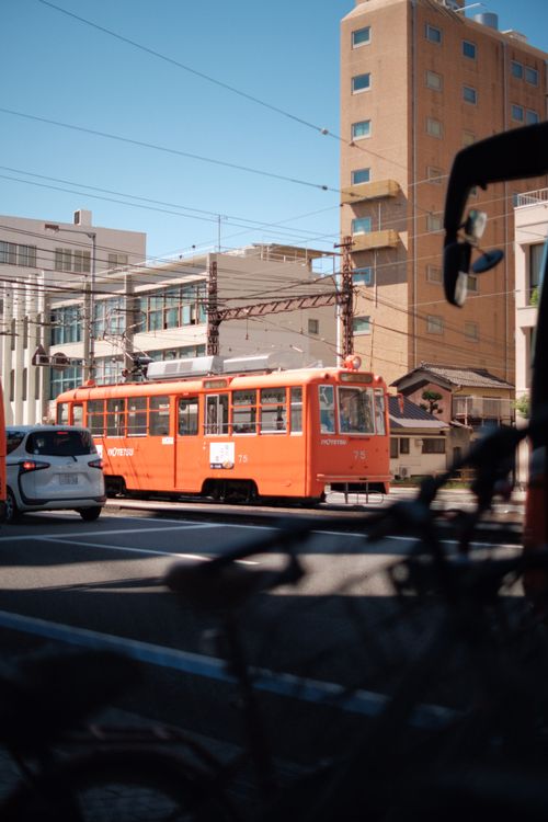 Free Red tram moves through urban area on sunny day alongside modern buildings. Stock Photo