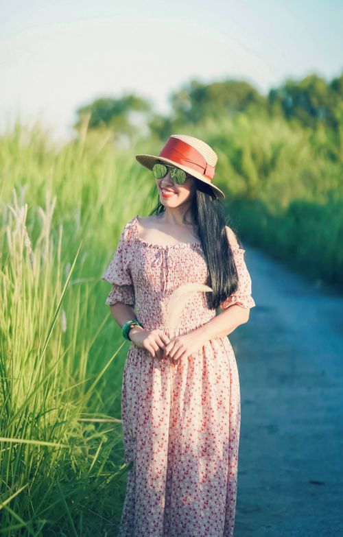 Free A woman wearing a floral dress and hat smiles brightly in a sunny outdoor setting. Stock Photo