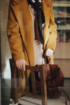 Close-up of a person holding a chair and bag indoors.