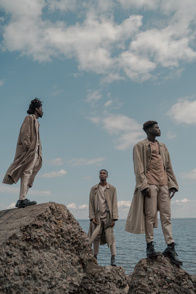 Men Dressed In Coats Standing On Cliff Rocks And Looking In Different Directions