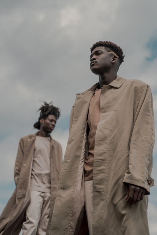 Free Artistic portrait of two men in long coats standing outdoors under a cloudy sky, serious expressions. Stock Photo