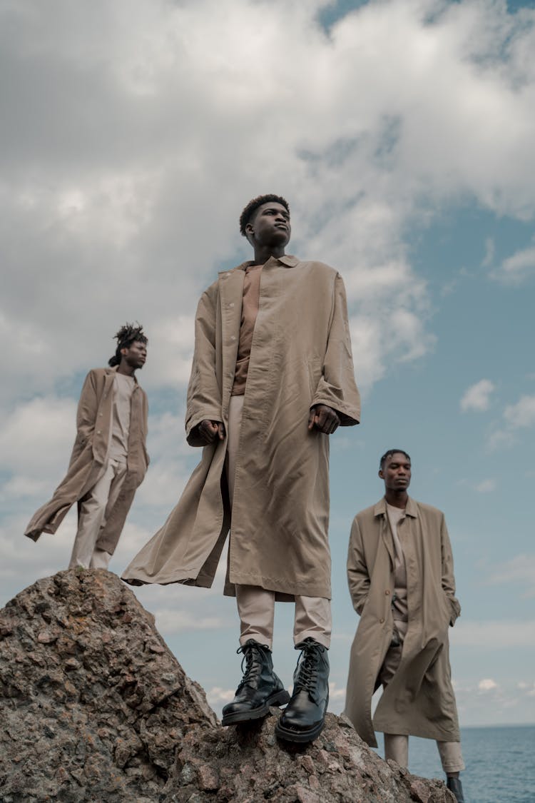 Small Group Of Men Dressed In Coats Standing On Cliff Rocks By Sea