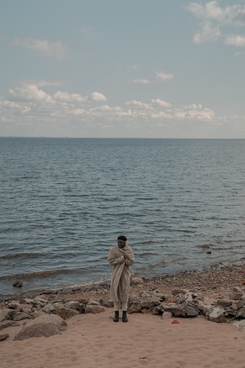 Man Standing Alone on Beach Wrapped in His Coat