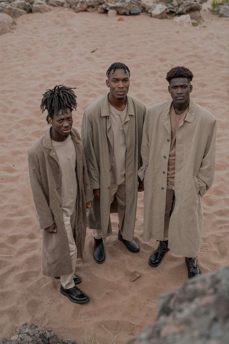 Three Men Wearing Identical Coats Standing On Sandy Beach