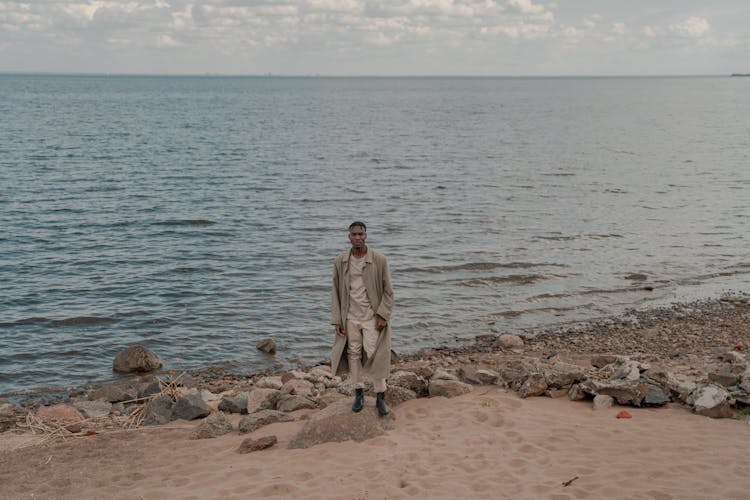 Lonely Man In Long Coat Standing On Rock On Beach Shore