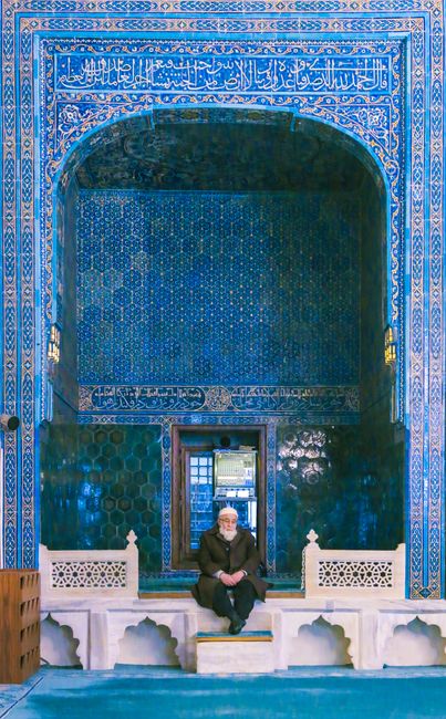 An elderly man sits in a richly decorated blue-tiled mosque in Turkey.