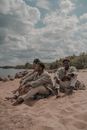 Small Group of Dressed Up Men Sitting Barefoot on Sandy Beach on Sunny Day