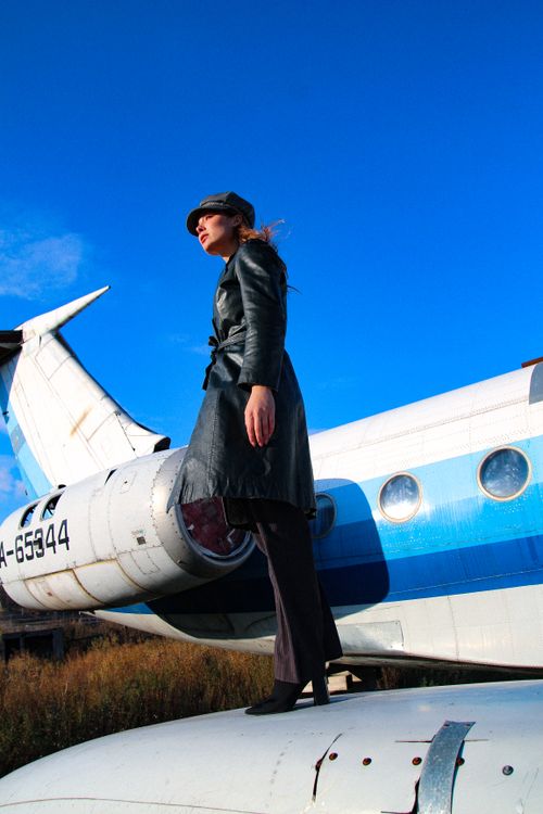 Free Fashionable woman in black coat poses on an aircraft wing on a sunny day in Russia. Stock Photo