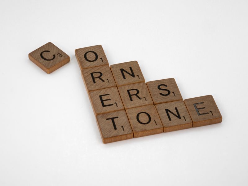 Close-up of Scrabble tiles spelling 'CORNERSTONE' on a white background.