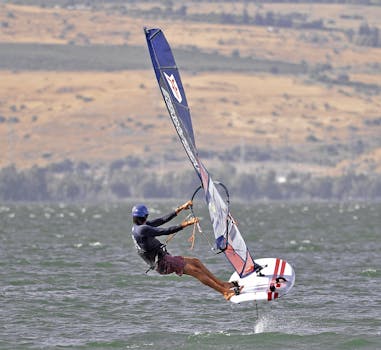 Dynamic windsurfing action on the Sea of Galilee in Tiberias, showcasing skill against a scenic backdrop.
