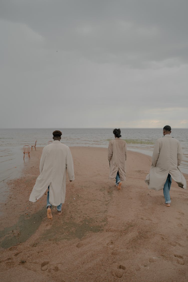 Men In Autumn Coats Walking Barefoot On Beach